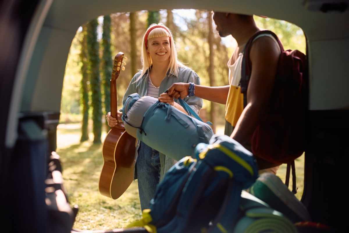 Zwei junge Reisende laden ihre Rucks&auml;cke am Auto im Wald, bereit f&uuml;r ihren Campingausflug.